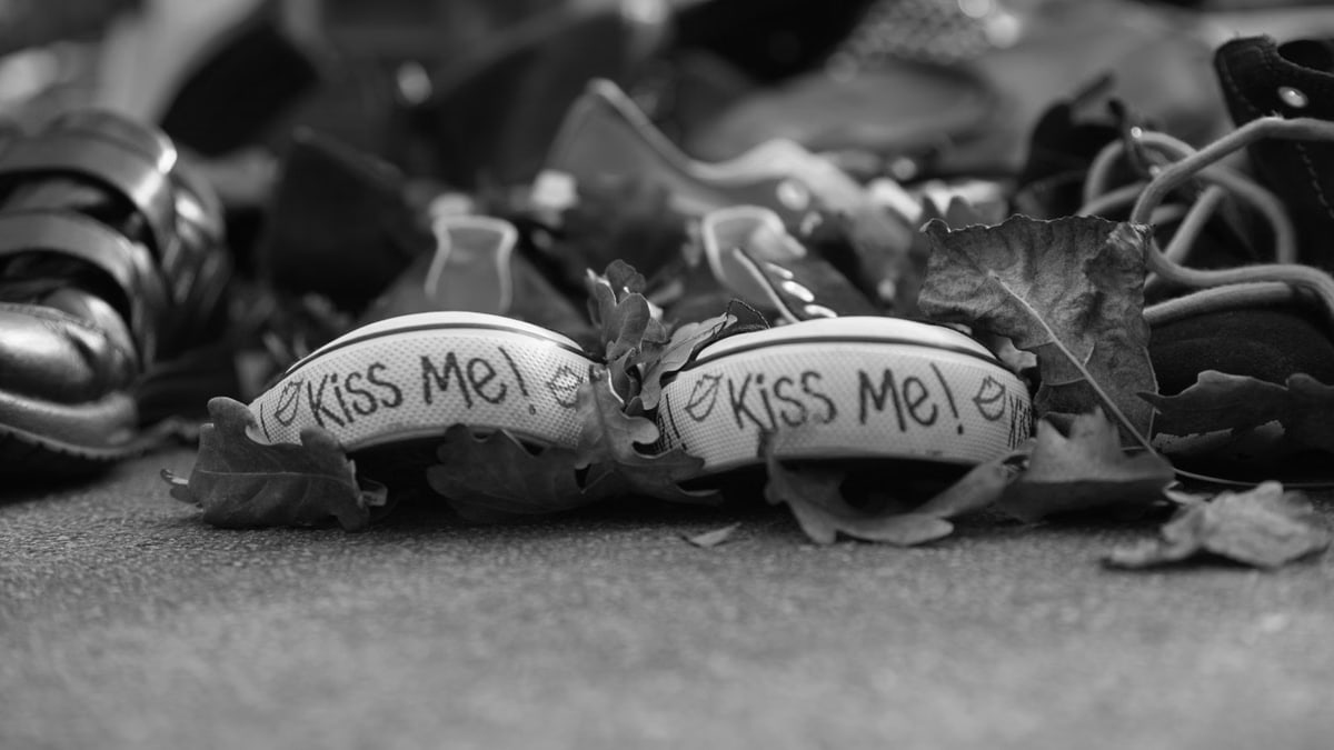 Black and white photo featuring a sneaker with 'Kiss Me' text, surrounded by autumn leaves.